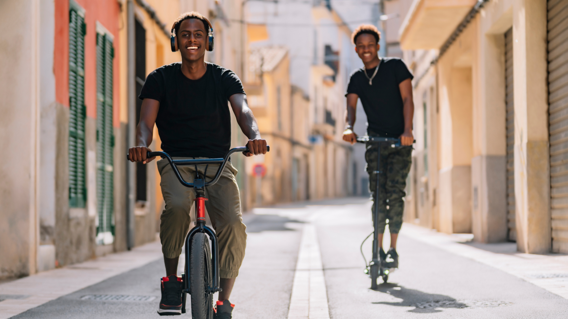 Two you males riding a bicycle and a electric scooter.