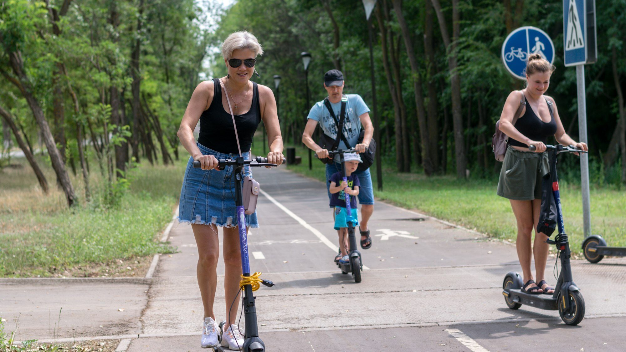 A group of young people rides electric scooters in the park on a summer day, can i ride electric scooter on sidewalk