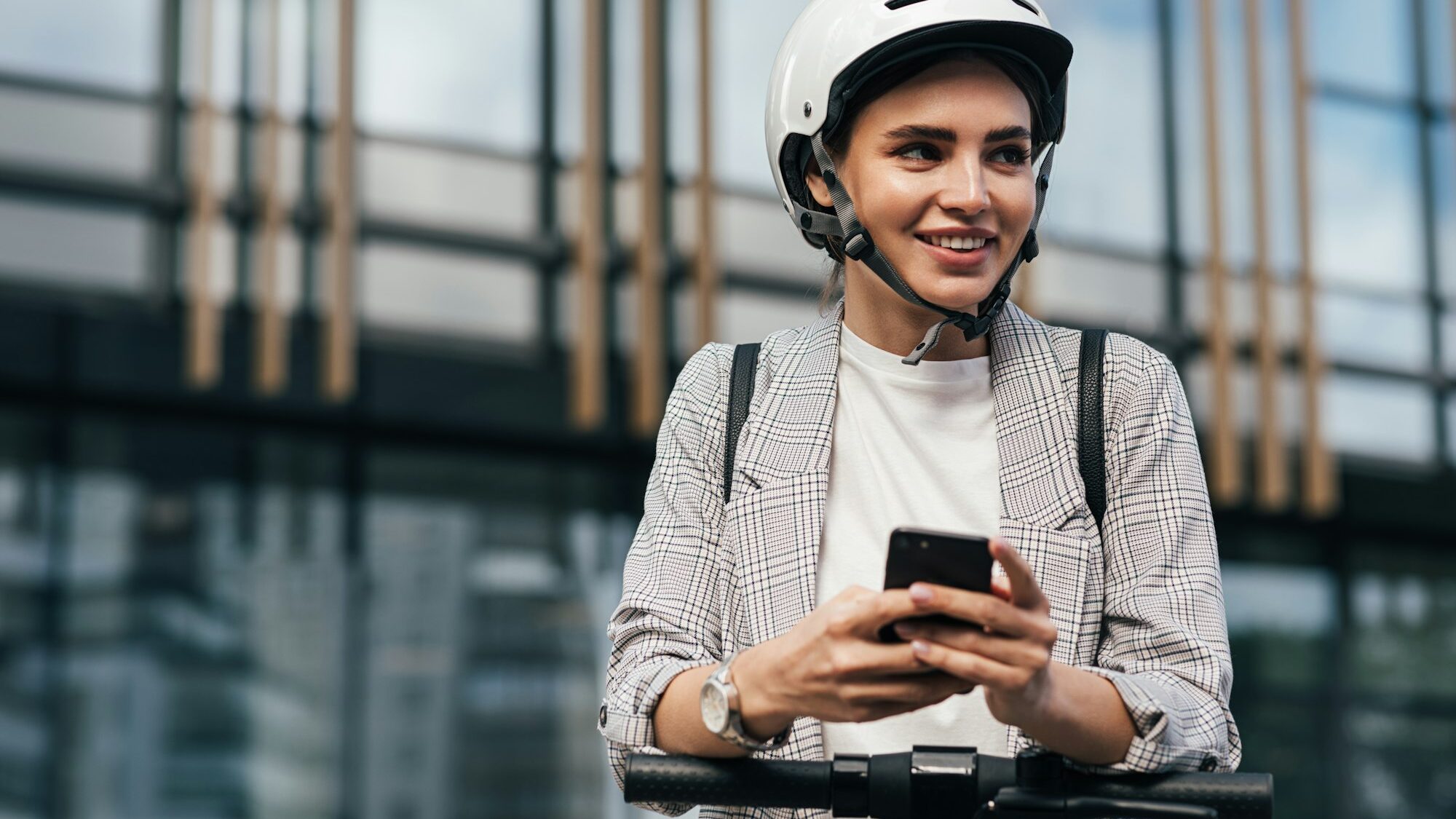 Cheerful woman in helmet using a mobile phone to unlock an electric scooter