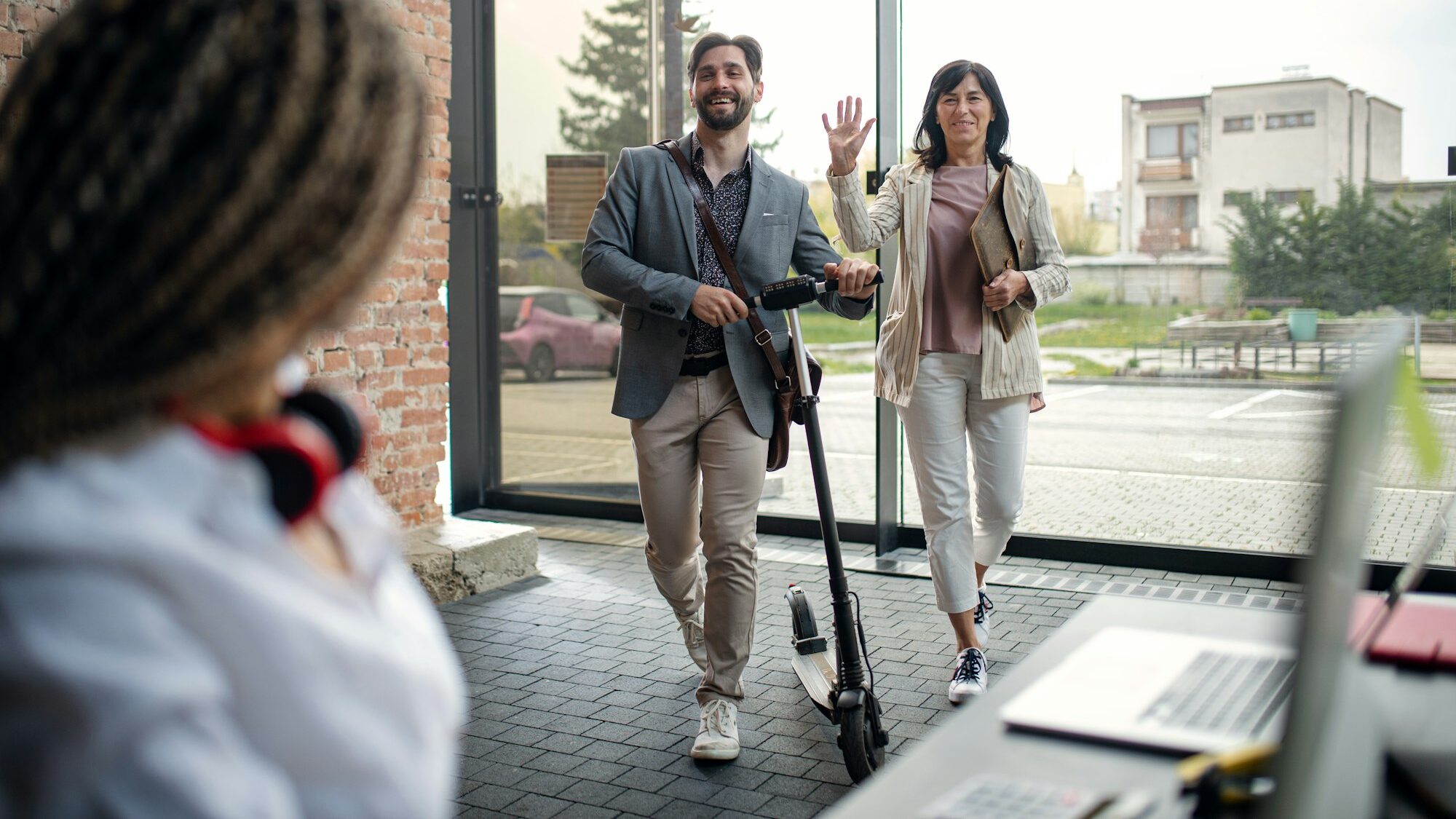 Young and old businesspeople with scooter entering office, coworking and eco commuting concept